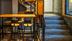 Un intérieur moderne avec un escalier en bois, un coin repas avec des tabourets et une bibliothèque.