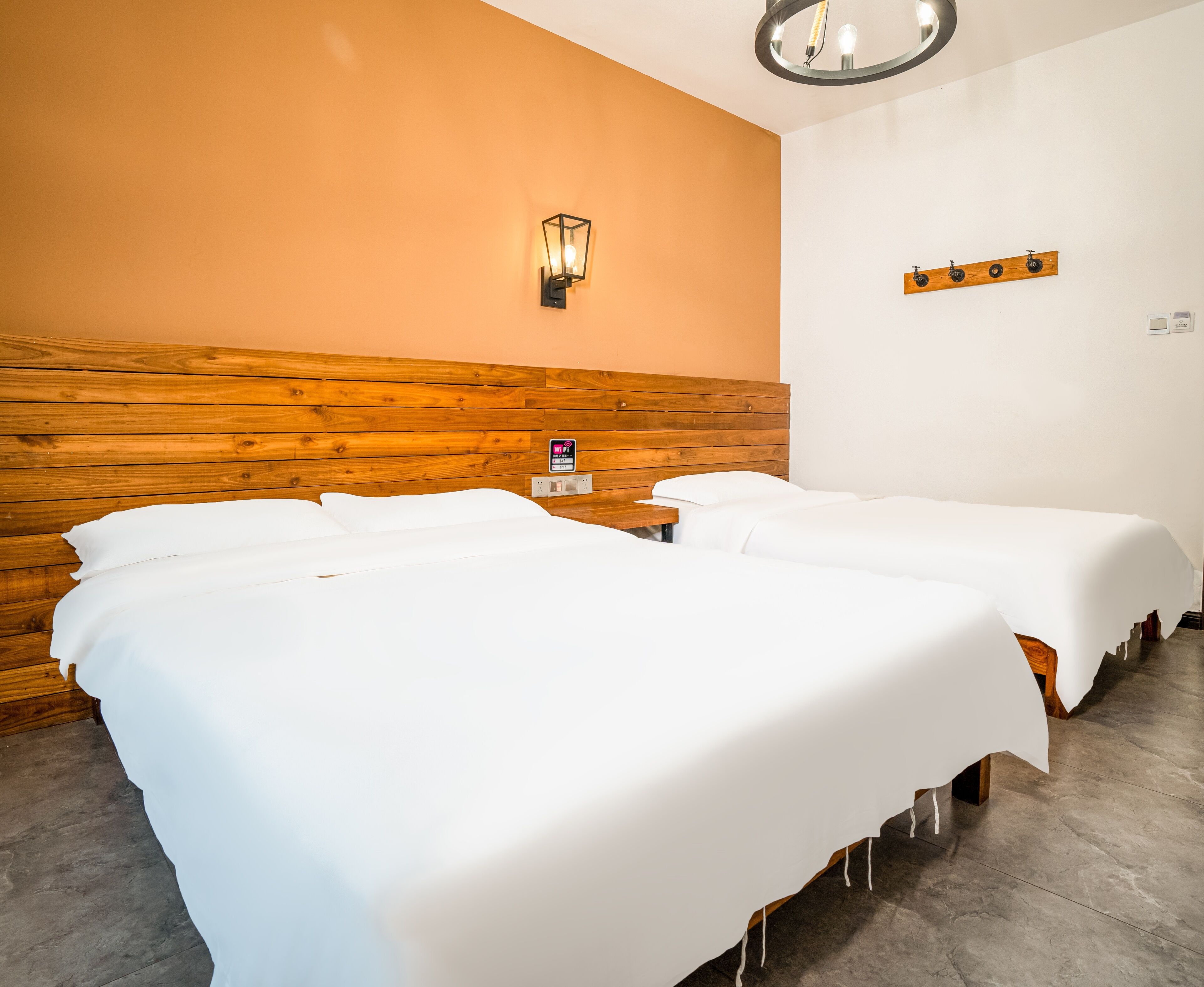 Hotellihuone, jossa on kaksi sänkyä, puinen pääty ja seinään kiinnitetty valaisin sekä pieni pöytä.