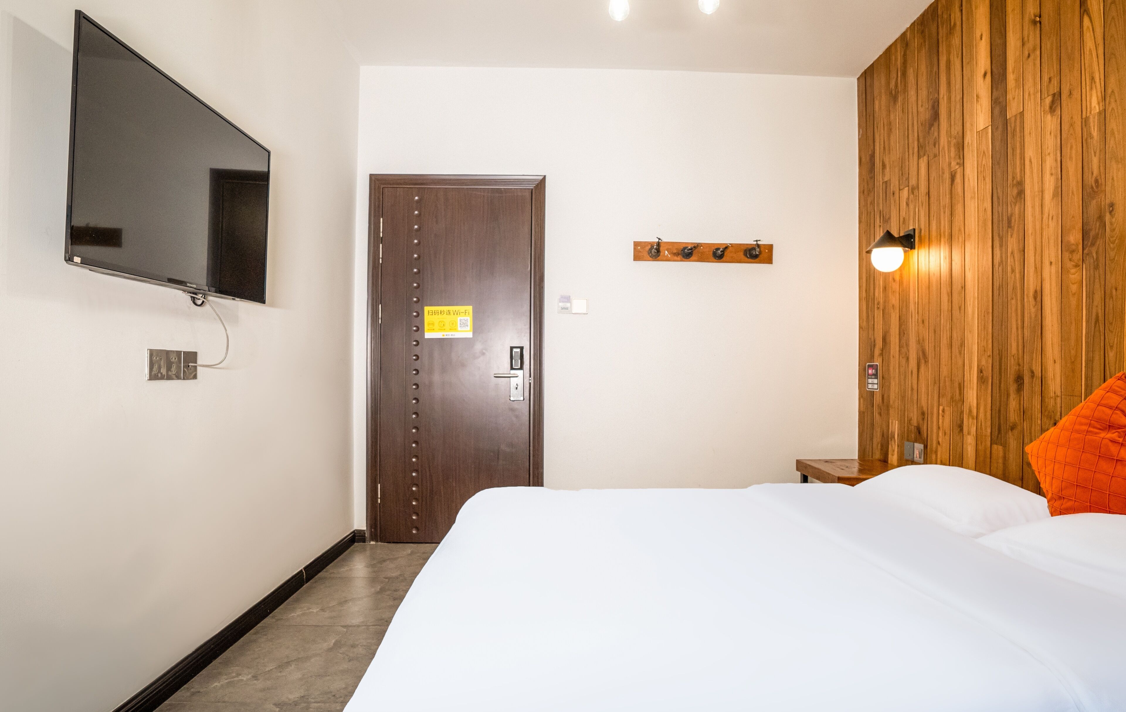 Habitación de hotel con cama, televisor montado en la pared, panel de pared de madera y una puerta con un letrero.