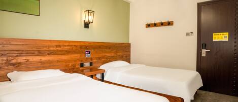 A hotel room with two single beds, a wooden headboard, a wall-mounted light, a door with a Wi-Fi sign, and a small table.