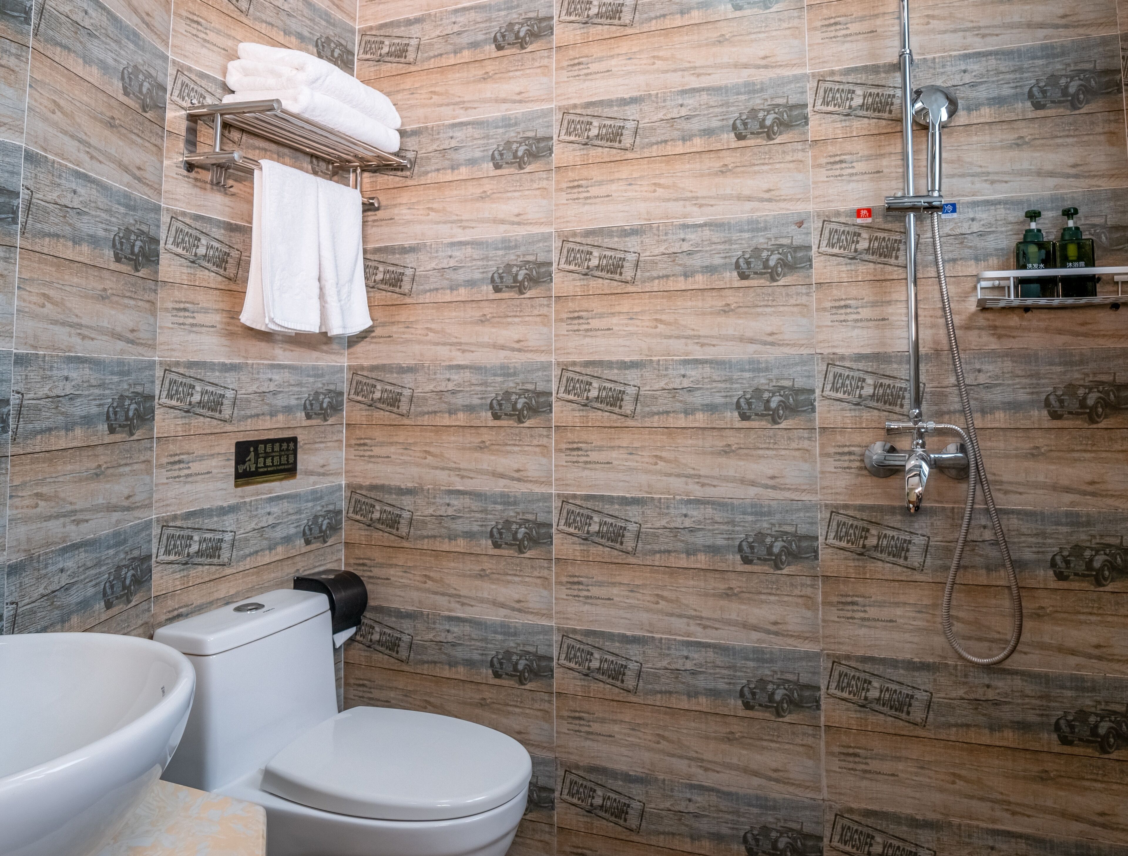 A bathroom with wooden wall tiles, a toilet, a sink, a towel rack, and a shower with a handheld showerhead.