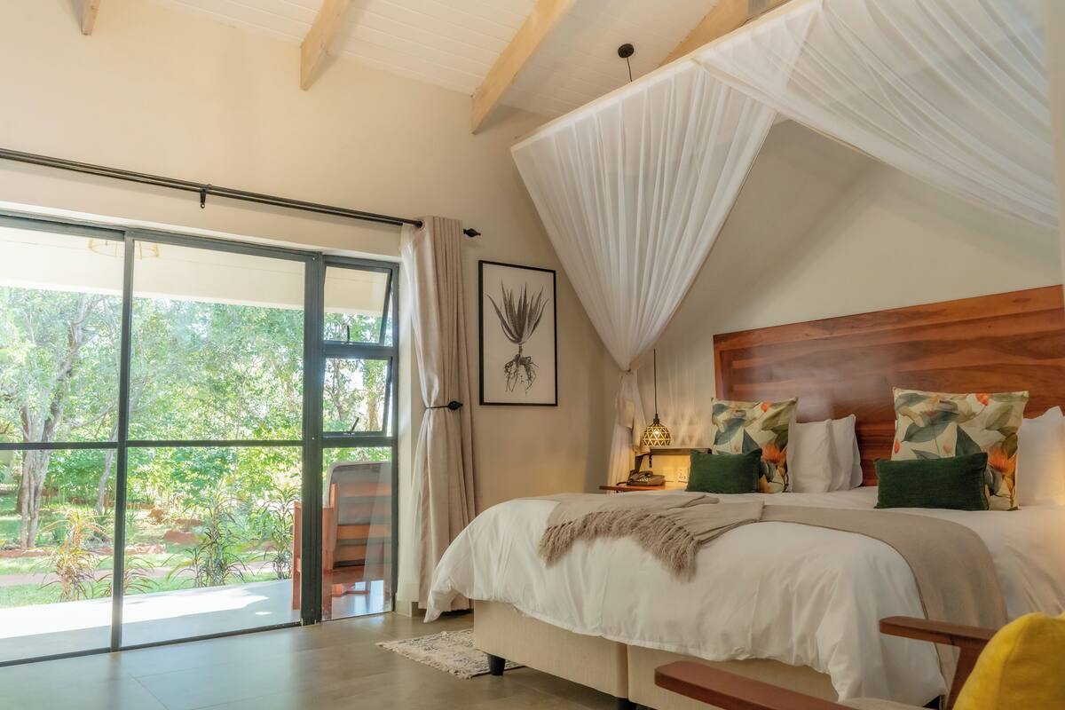 Quarto com uma grande porta de correr de vidro que dá para um jardim, uma cama com dossel e cabeceira de madeira.