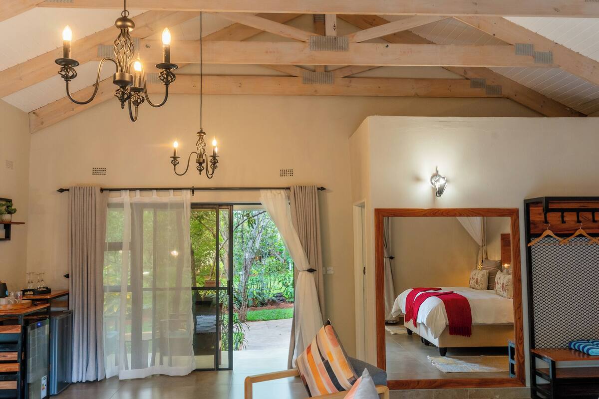 Quarto de hotel com cama, área de refeições com mesa e cadeiras, um candelabro e vista para o exterior.