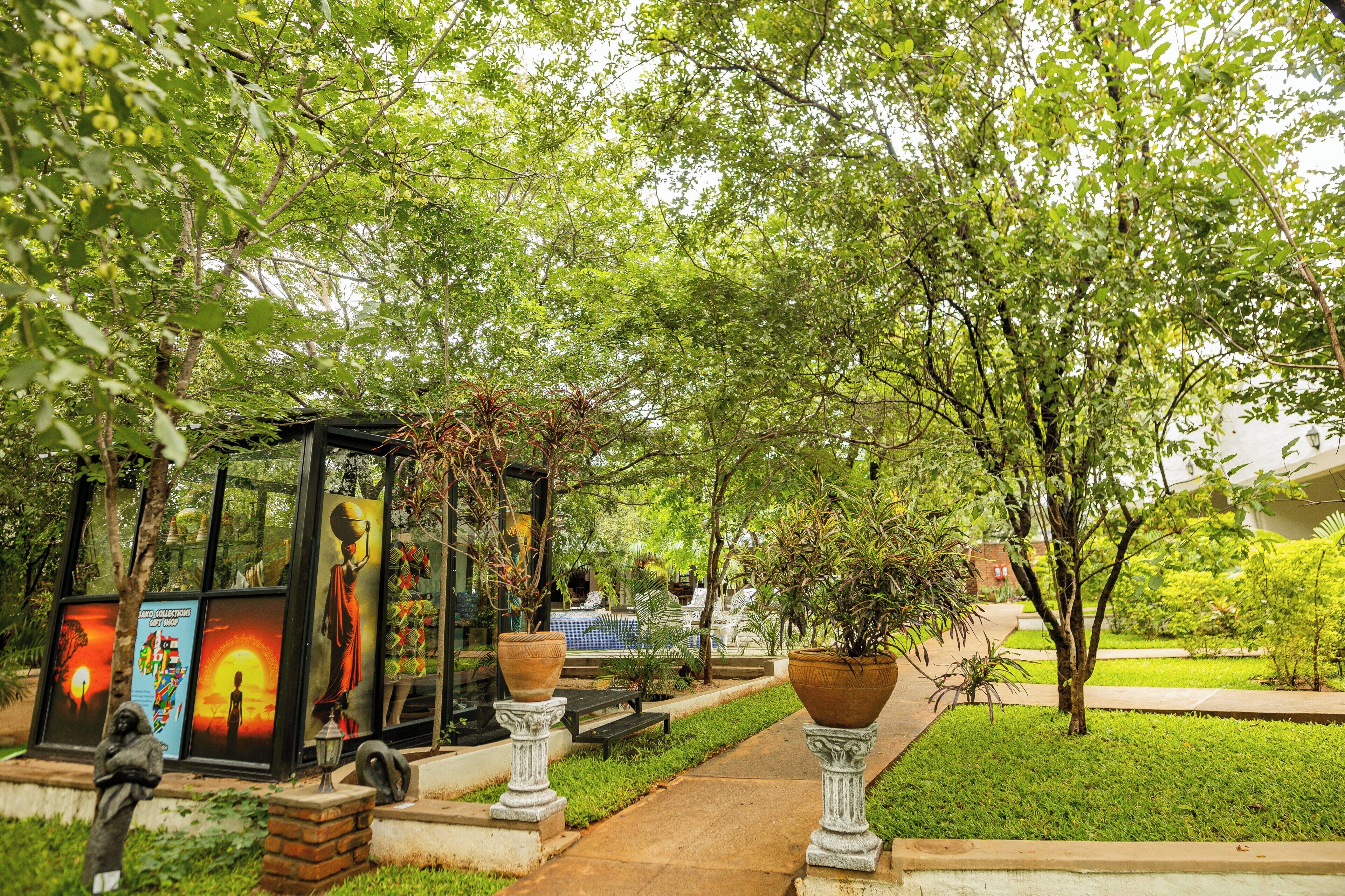 A garden area with a glass structure displaying artwork, potted plants, and a pathway.