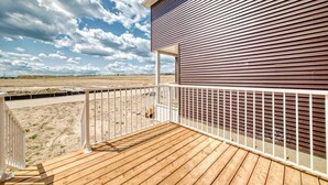 A wooden deck with a white railing overlooking a sandy beach and a building with horizontal siding. - New house to stay in Calgary close to Airport and the big mall Crossiron Mill (Calgary)