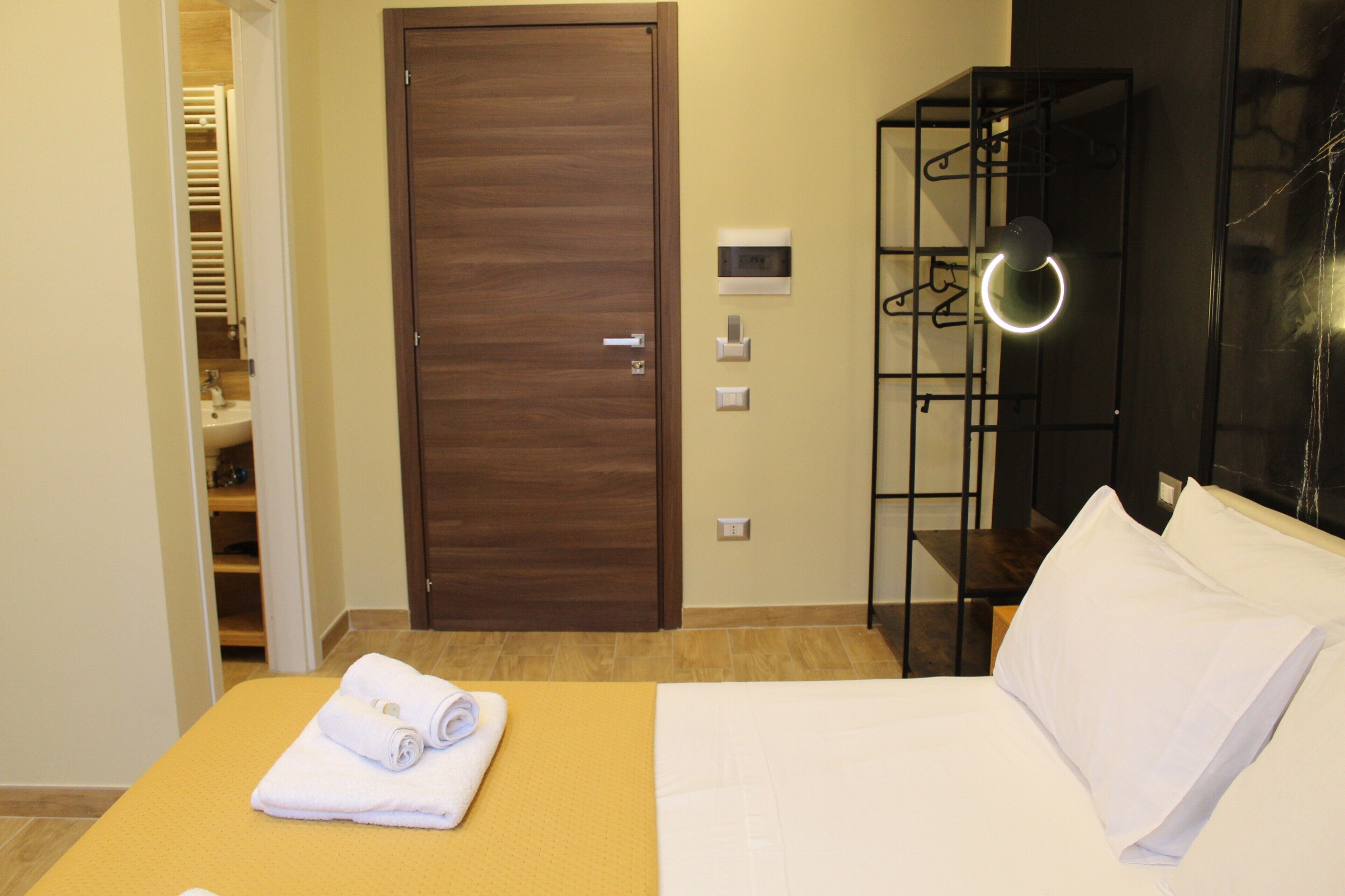 A hotel room with a bed, a wardrobe, a bathroom, and a shelf with clothes.