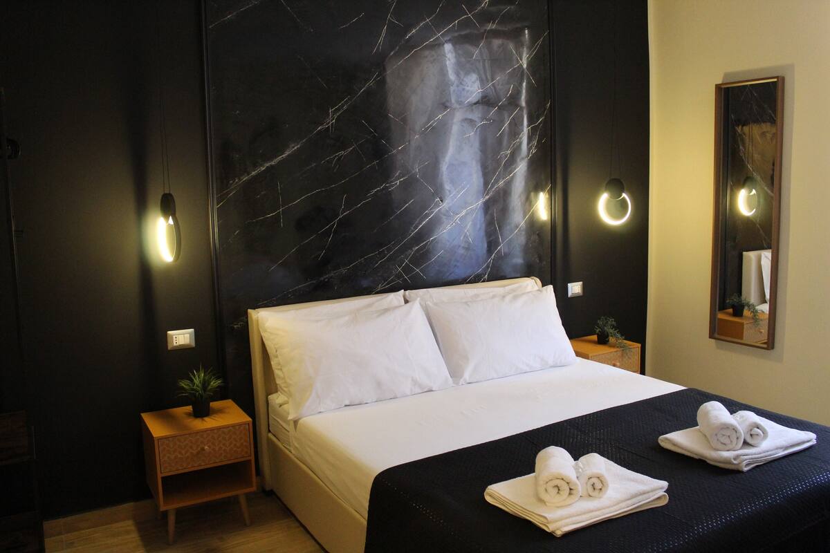 Ein Hotelzimmer mit einem großen Bett, einem Nachttisch mit Pflanze und einem Spiegel an der Wand.