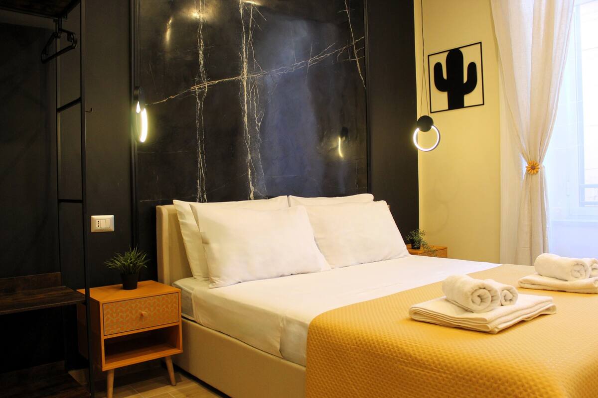 Ein Hotelzimmer mit Bett, Nachttisch, einer Topfpflanze und einer Kakteedeko an der Wand.
