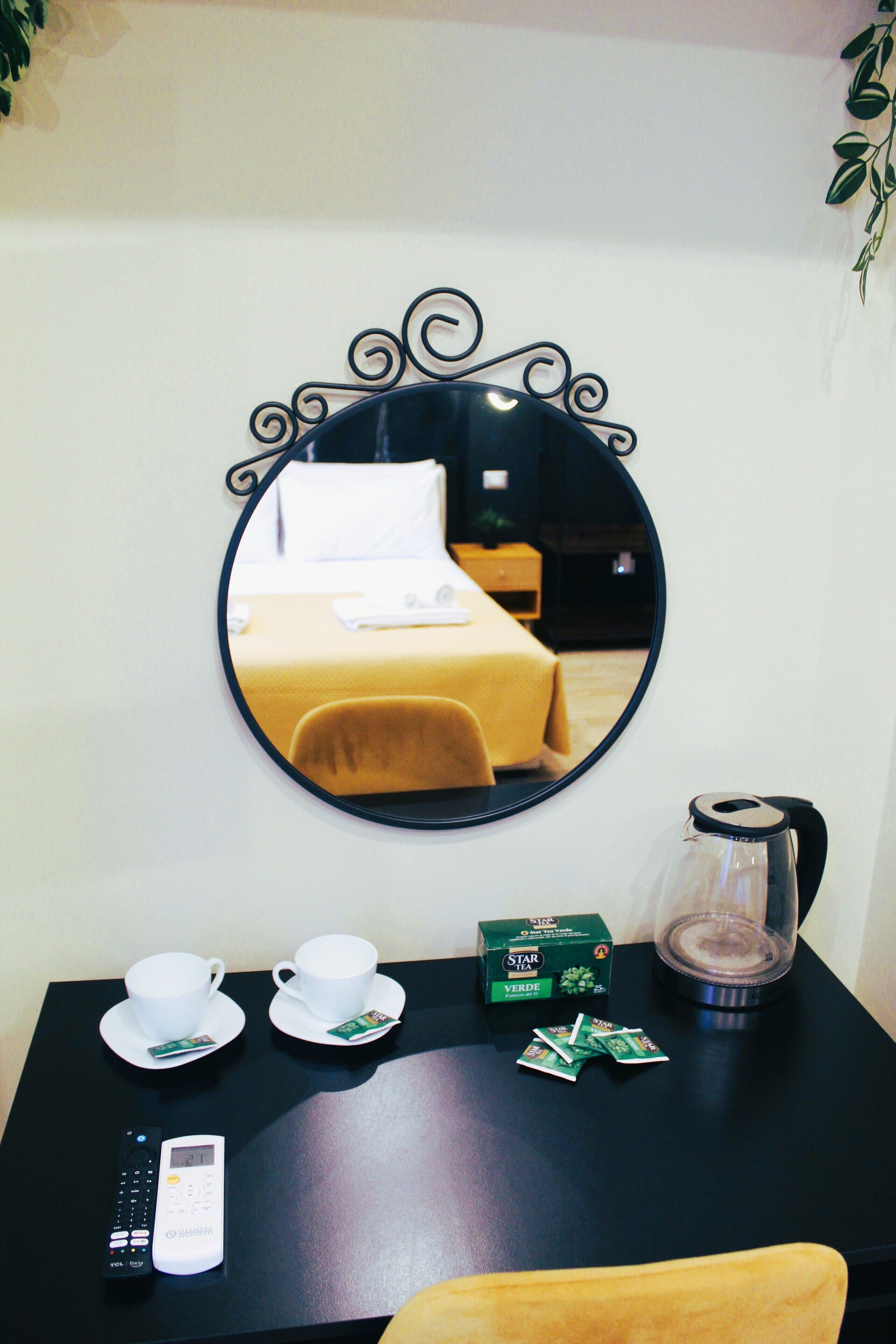 A hotel room with a bed, a bedside table with a coffee maker, cups, and a remote control.