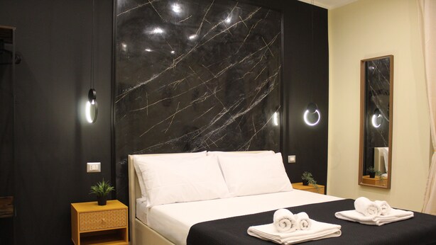 Ein modernes Hotelzimmer mit einem großen Bett, einem Nachttisch mit Pflanze und einem Spiegel an der Wand.