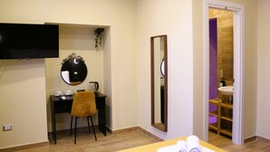 Ein Hotelzimmer mit Flachbildfernseher, Schreibtisch mit Stuhl, Spiegel und angrenzendem Badezimmer.