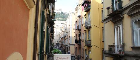 A narrow street with buildings on either side, a signboard for a bed and breakfast, and a view of a hill in the distance.