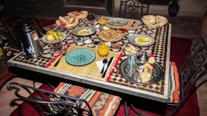 Une table à manger dressée avec différents plats, notamment du pain, des fruits et une théière.