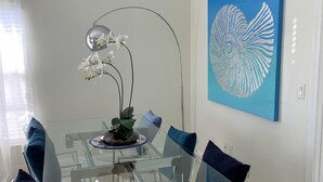 A modern dining area with a glass table, blue chairs, a decorative orchid, and a wall art of a bird. - House - Sleeps 6 - Hot Tub - Garden - Near Beach (Naples)