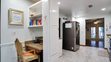 Een keuken met een koelkast, een eettafel met stoelen en een boekenkast vol boeken.