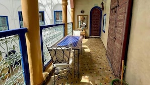 Un couloir étroit au sol carrelé, une table avec des chaises et une grande porte en bois.