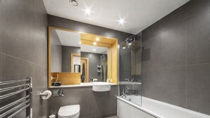 Un bagno moderno con doccia vetrata, vasca da bagno bianca e un mobile vanitario in legno con specchio.