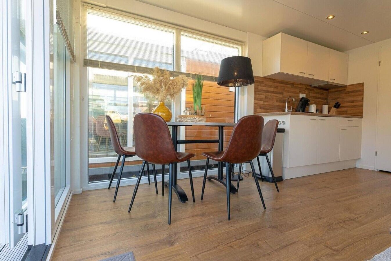 Una cucina moderna con zona pranzo, con un tavolo e sedie, una lampada e vista panoramica attraverso ampie finestre.