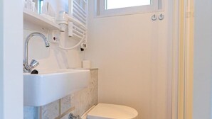 Un baño pequeño con lavamanos, inodoro y una ventana sobre la puerta.