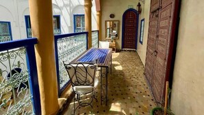 Un pasillo estrecho con suelo de baldosas, una mesa con sillas y una puerta de madera grande.