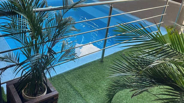 Zona de piscina en la azotea con césped artificial, plantas en macetas y barandilla metálica.