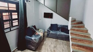 Una habitación con ventilador de techo, una escalera, un sofá y un televisor instalado en la pared.