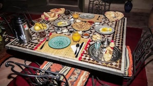 Ein Esstisch ist reichhaltig mit Speisen gedeckt, darunter Brot, Früchte und eine Teekanne.