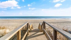 Een houten looppad dat naar een strand leidt, onder een heldere lucht.