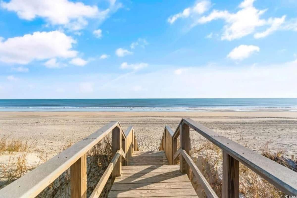 Une promenade en bois qui mène à une plage, sous un ciel dégagé.