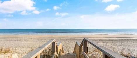 A wooden boardwalk leading to a beach with a clear sky.