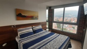 Ein Schlafzimmer mit einem großen Bett, Blick auf die Stadt durch ein Fenster und einem Gemälde an der Wand.