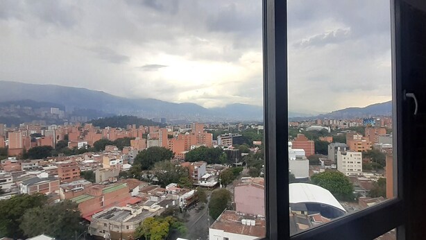 A cityscape viewed from a high-rise window, featuring a dense urban area with various building types and a distant mountain range. - Laureles Penthouse rooftop Suite (Medellín)