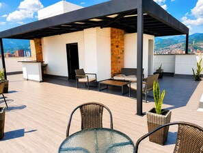 A rooftop terrace with a covered seating area, a bar, and potted plants.