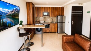 A compact kitchen with wooden cabinets, a stainless steel refrigerator, a built-in oven, and a microwave. - Laureles Penthouse rooftop Suite (Medellín)