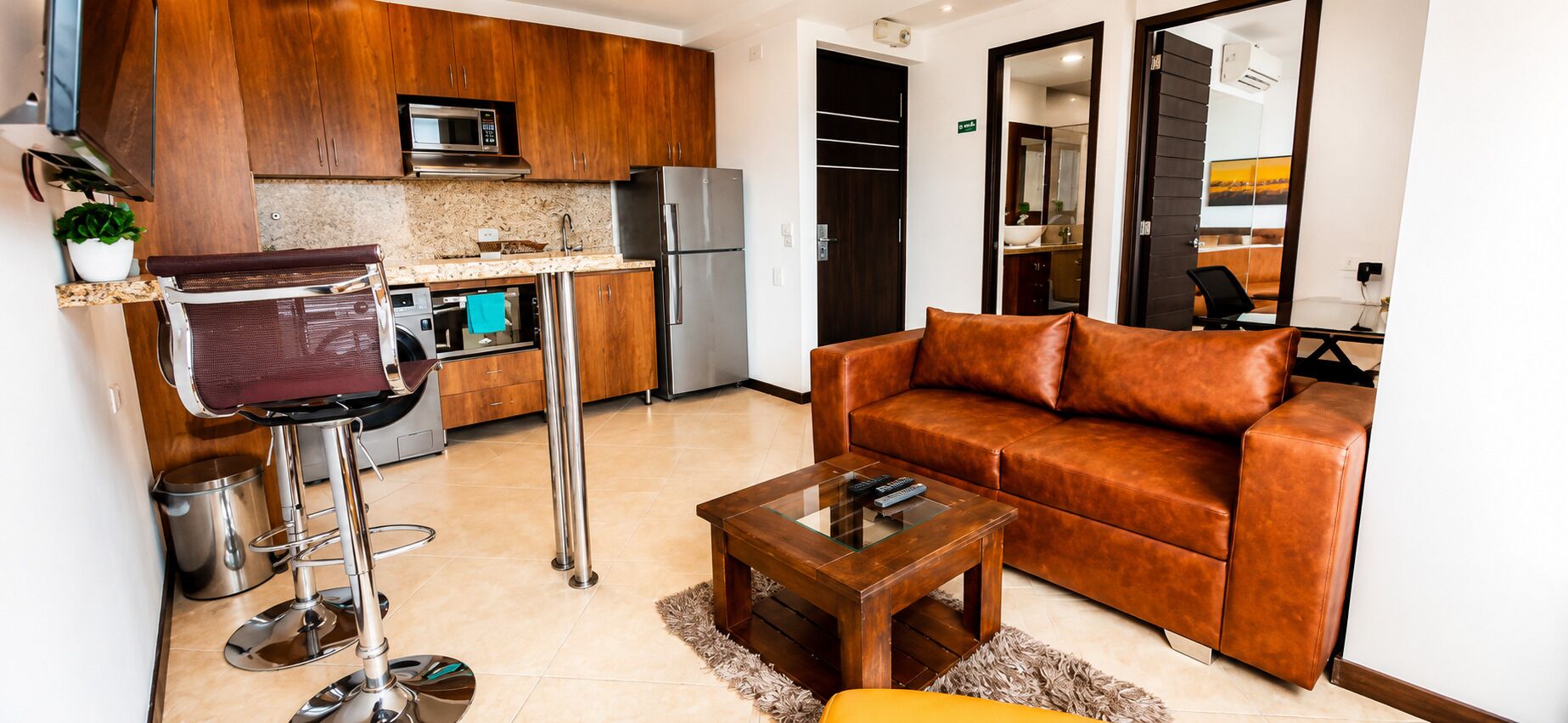 Um espaço de estar compacto com cozinha compacta, sofá de couro, mesa de centro e um banquinho de bar.