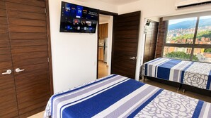 A hotel room with a large wardrobe, a television mounted on the wall, and a bed with a striped bedspread. - Laureles Penthouse rooftop Suite (Medellín)