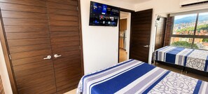 Una habitación de hotel con un armario grande, un televisor montado en la pared y una cama con colcha a rayas.