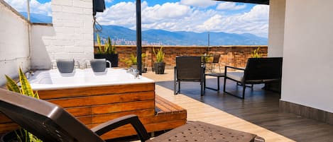 Una terraza en la azotea con un banco de madera, una bañera de hidromasaje y una mesa con sillas.