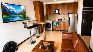 A compact living space with a kitchen, a seating area, and a TV displaying a mountain landscape. - Laureles Penthouse rooftop Suite (Medellín)