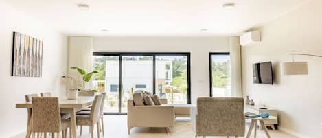 A modern living room with a dining area, a sofa, and a TV mounted on the wall.