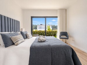 Une chambre moderne avec un grand lit, une vue sur l’extérieur et un fauteuil.