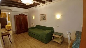 Una habitación con piso de madera, un sofá verde, un armario de madera, una mesita pequeña y una lámpara fijada a la pared.