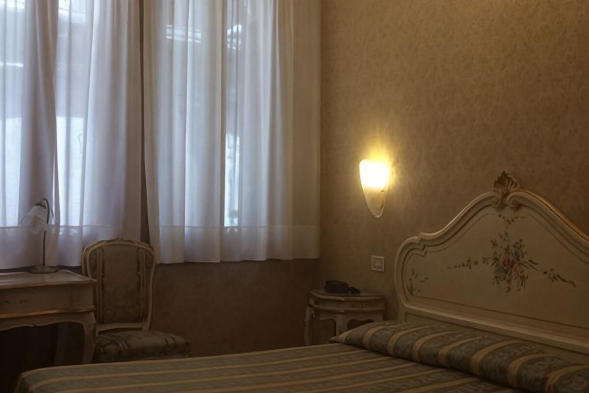 A hotel room with a bed, a chair, a desk, and a nightstand.