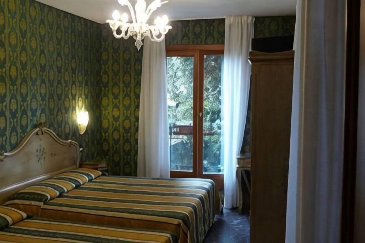 Un dormitorio con cama doble, candelabro, ventana con cortinas y vistas al exterior.
