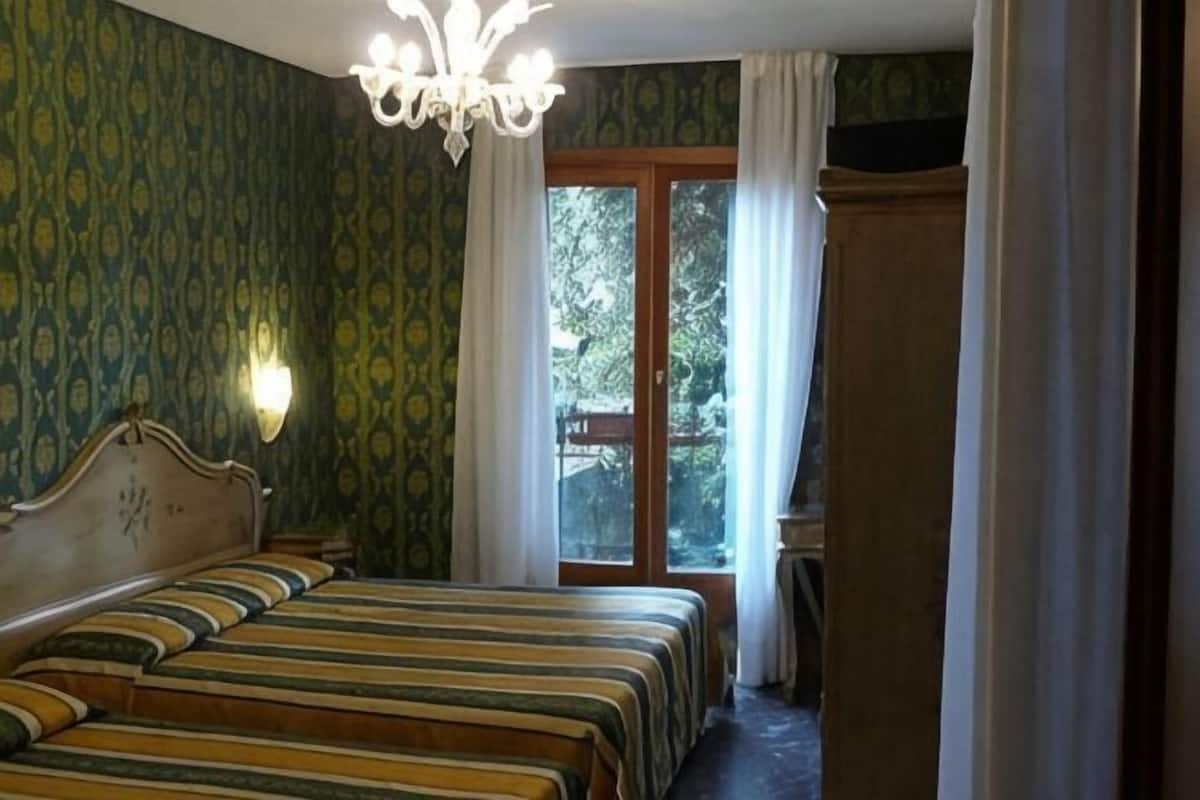 A bedroom with a double bed, a chandelier, a window with curtains, and a view of the outdoors.
