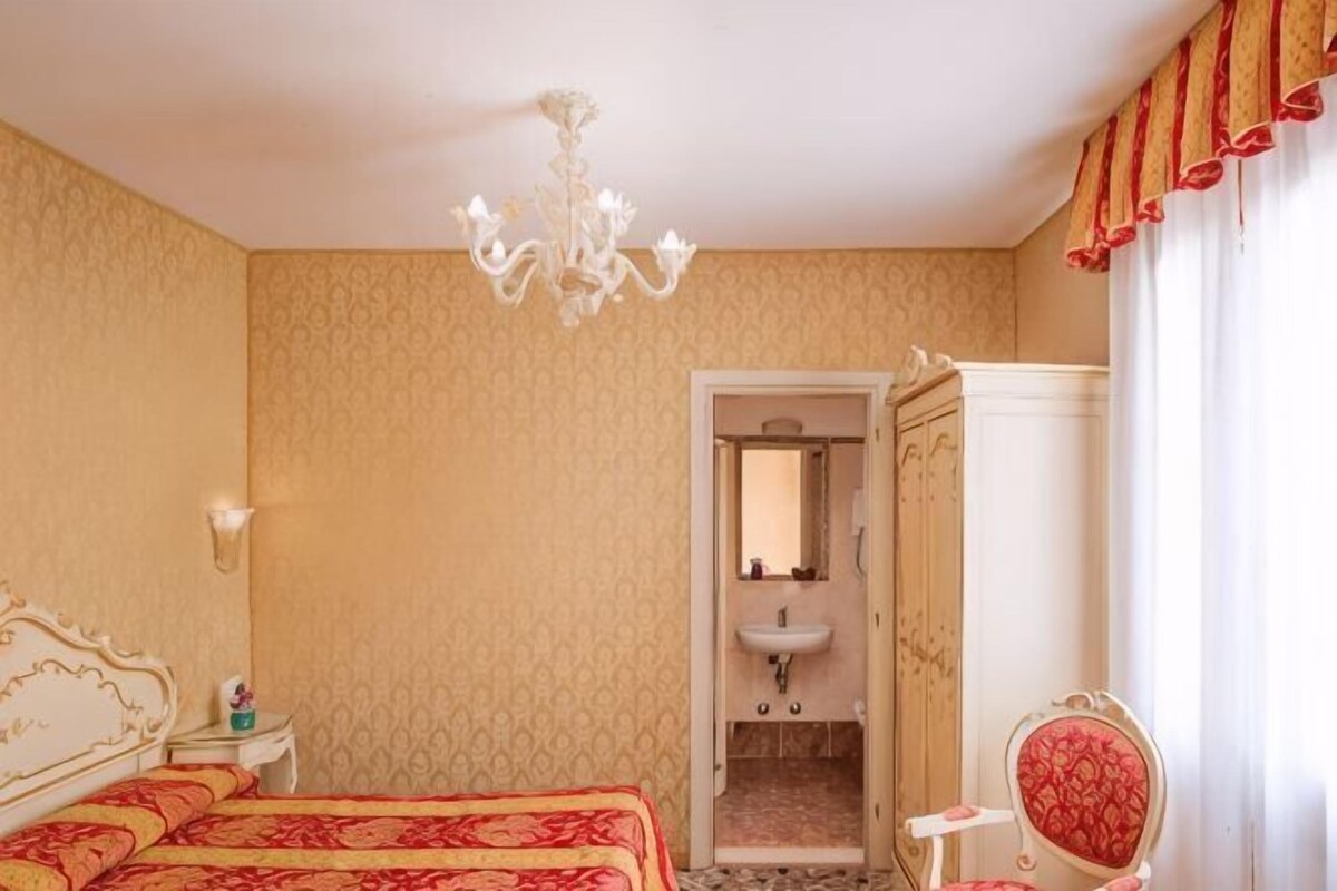 Una habitación de hotel con cama, tocador con espejo, candelabro y ventana con cortinas.