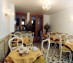 Un espace repas comprenant plusieurs tables et chaises, un lustre et une porte donnant sur une autre pièce.