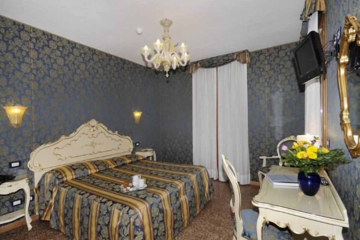 Una habitación de hotel con una cama doble, un escritorio con un florero, un televisor y un candelabro.