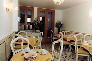 Un comedor con sillas blancas y manteles amarillos, un candelabro y vistas a través de una puerta.