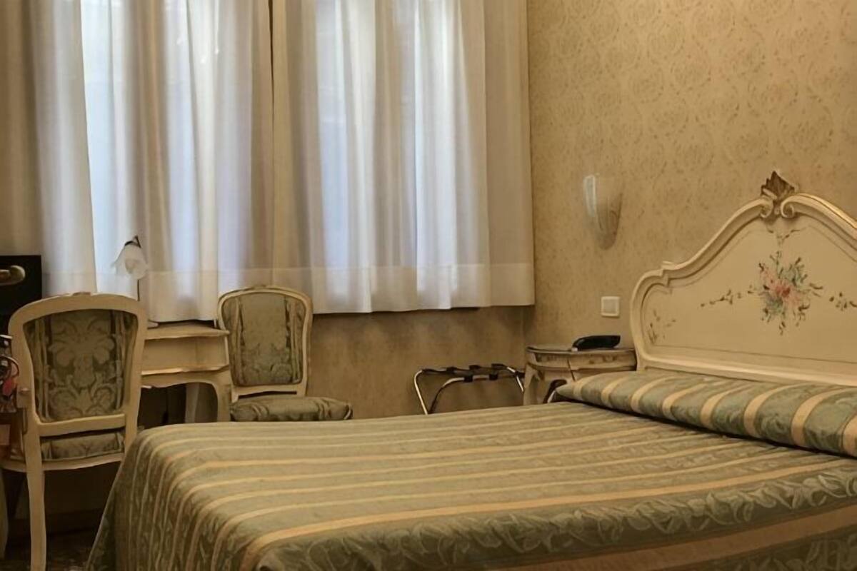 Una habitación de hotel con una cama, dos sillas, un escritorio y una mesita de noche.